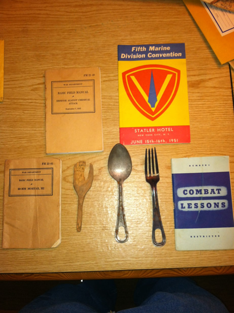 Carl Padovano's field utensil's from Iwo Jima. Field manuals surround them and Fifth Marine booklet in red yellow